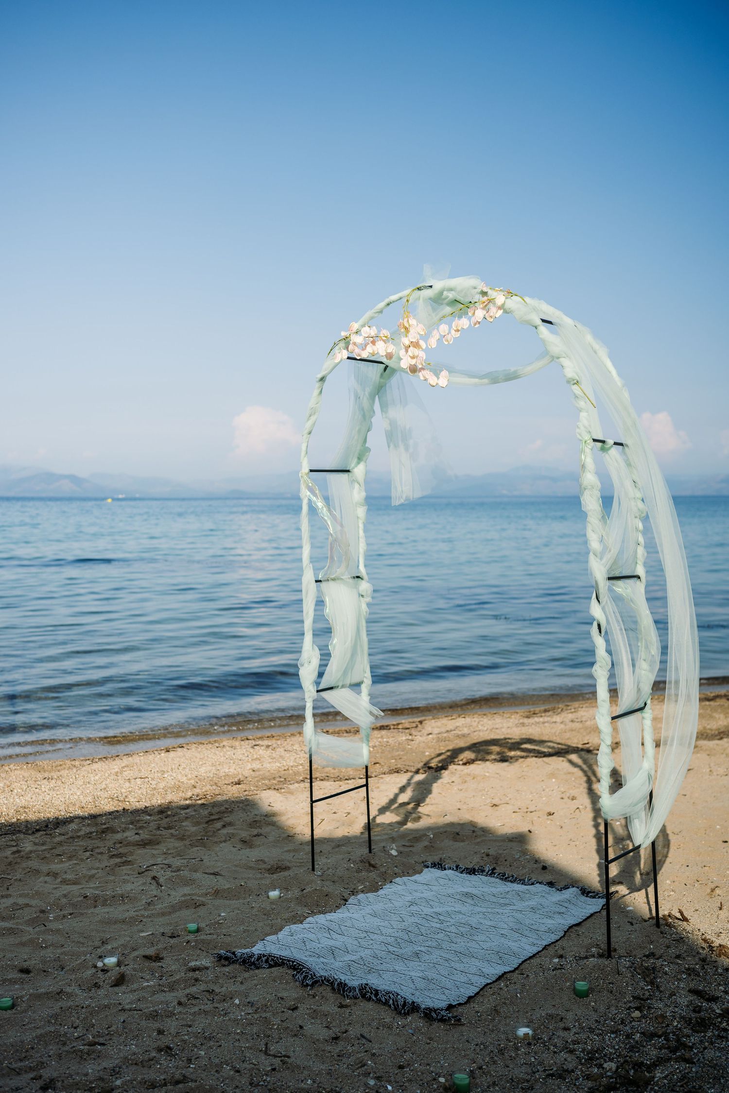 Beach wedding arch decorated with flowing fabric and flowers against blue ocean waters.