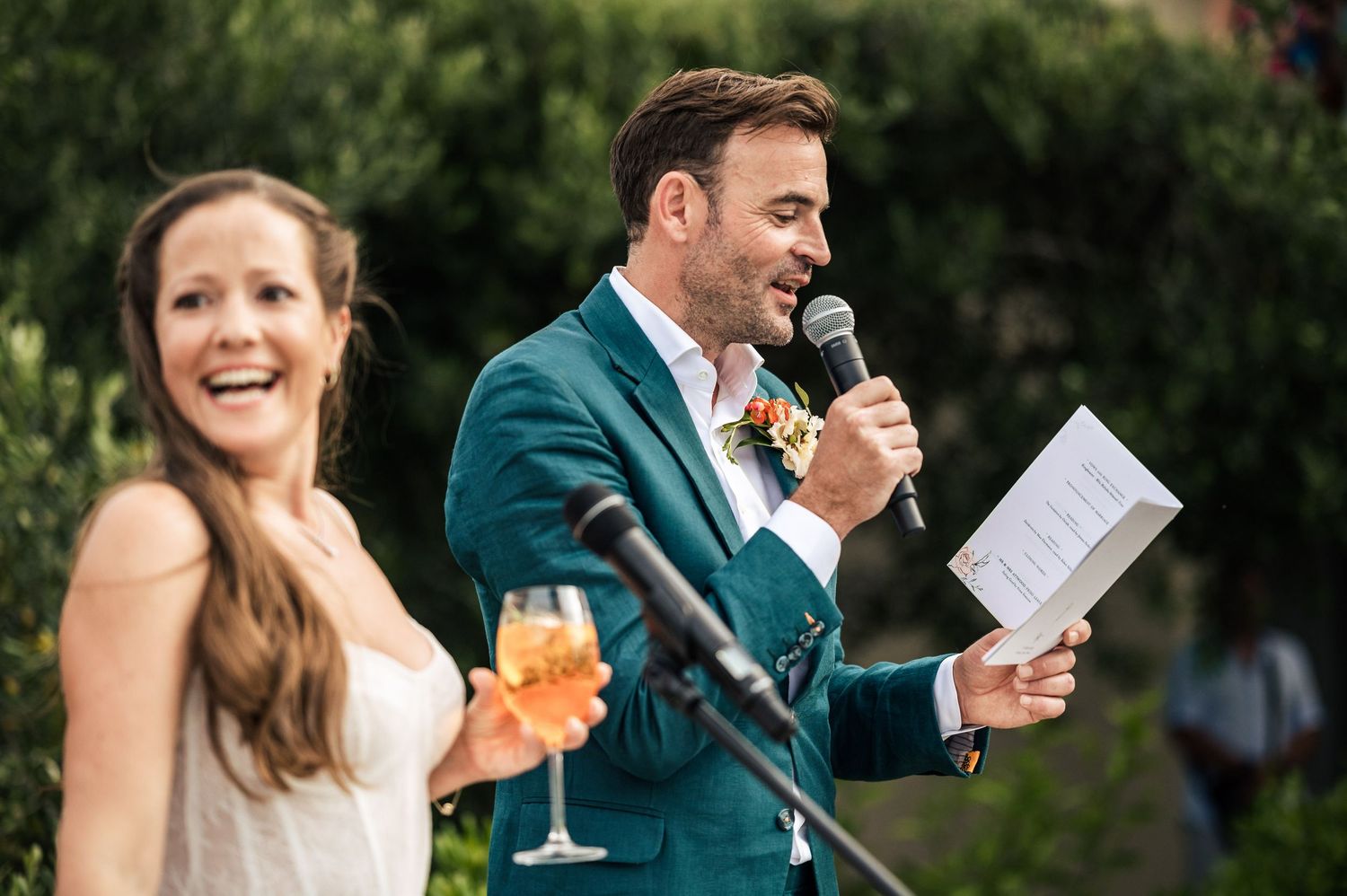 Wedding celebration speech moment with drinks and laughter in an outdoor garden setting.