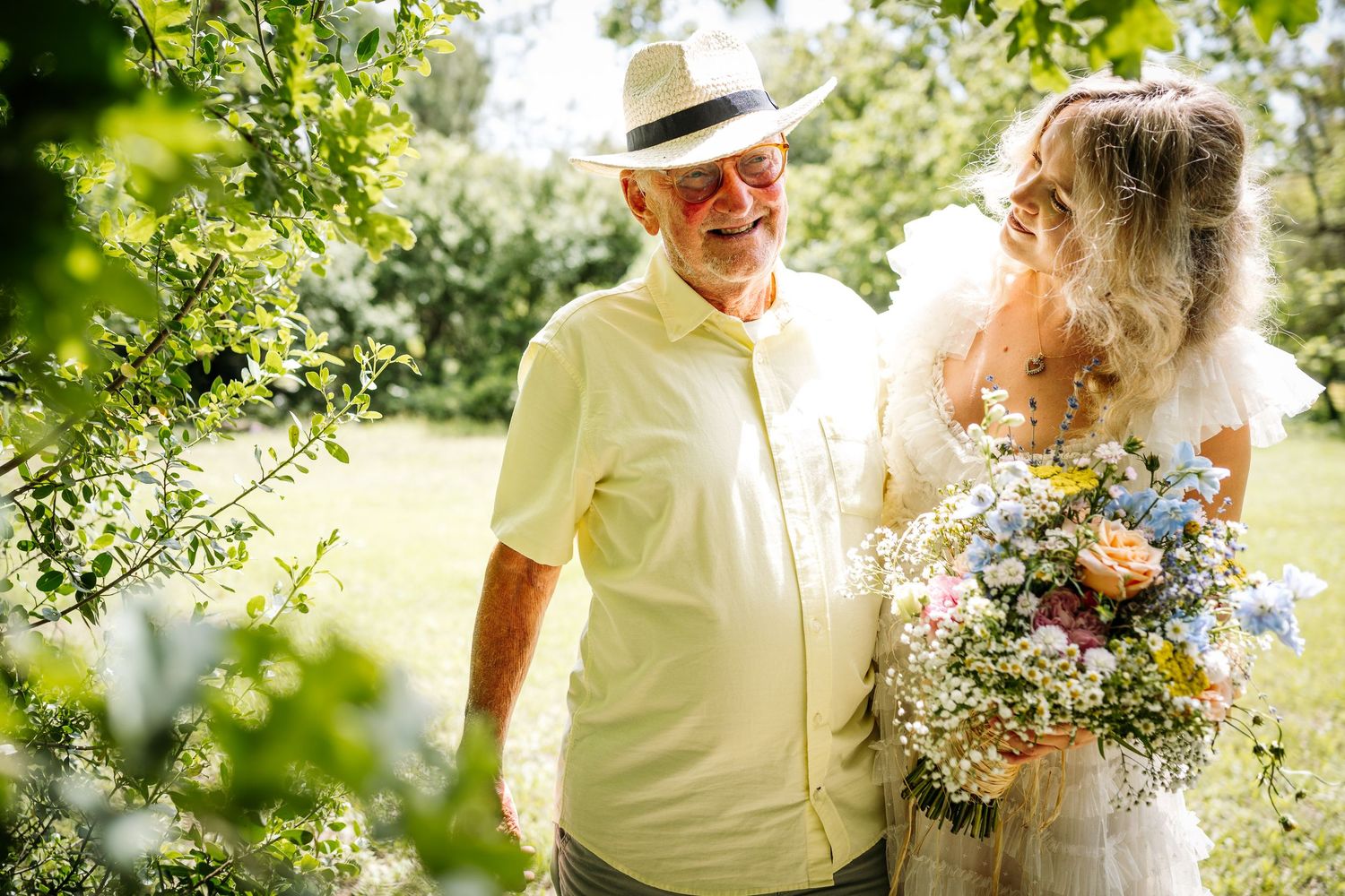 Sunny outdoor gathering with people walking through a garden path carrying flowers.