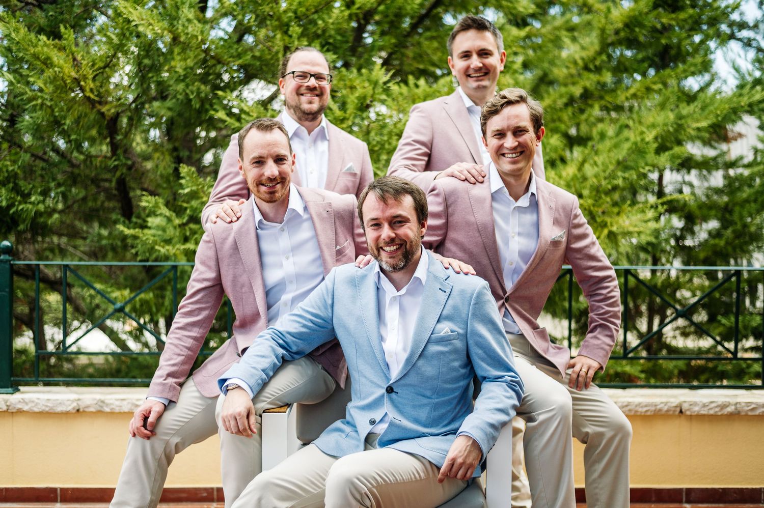 Group photo of wedding party in light blue and pink suits outdoors.