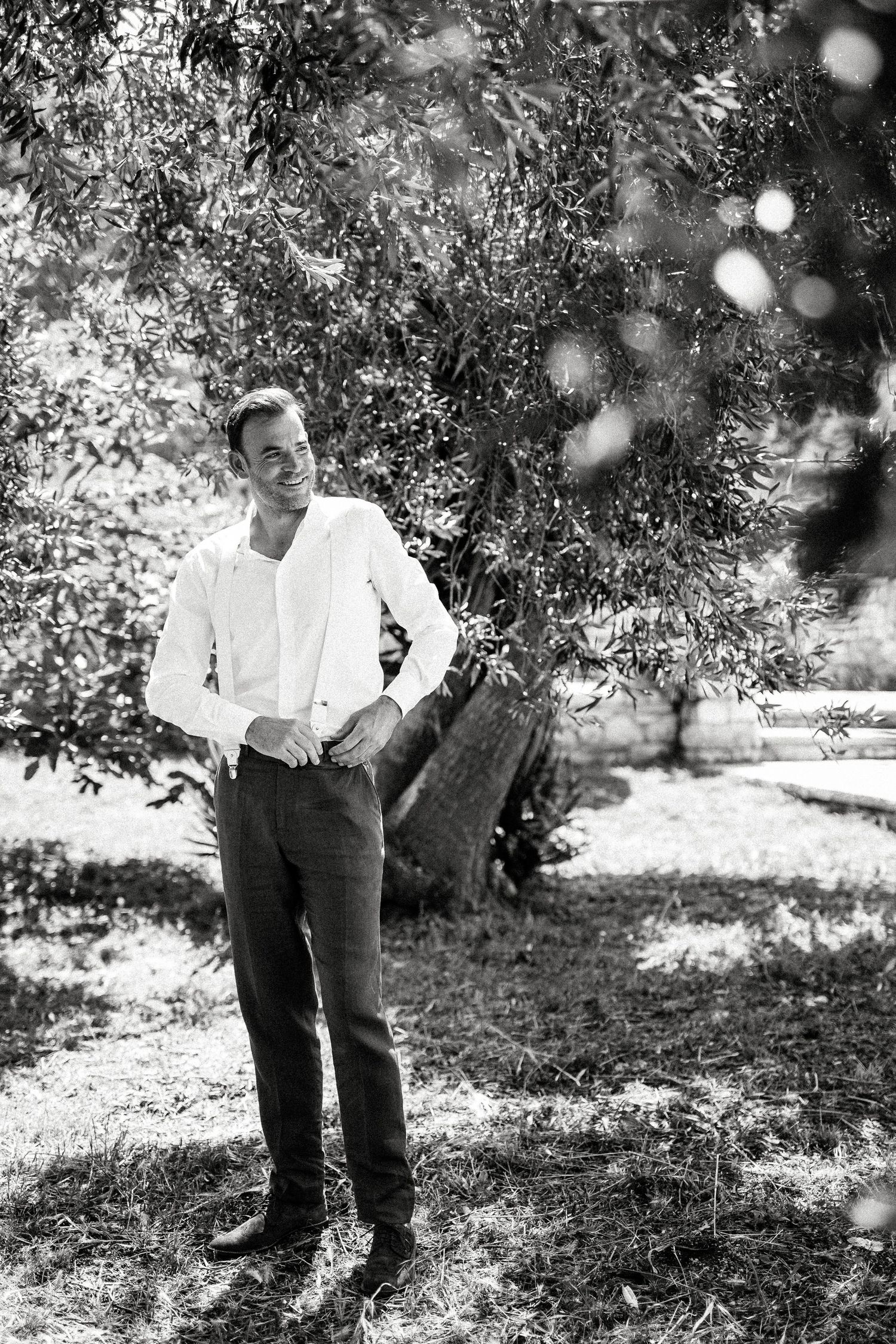 Black and white photograph of people in an olive grove with dappled sunlight.