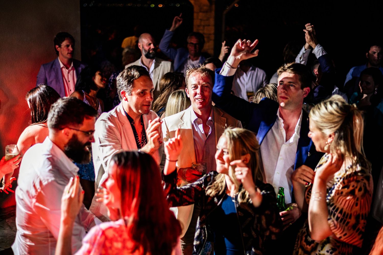 Dance floor filled with party guests under dramatic red lighting effects.