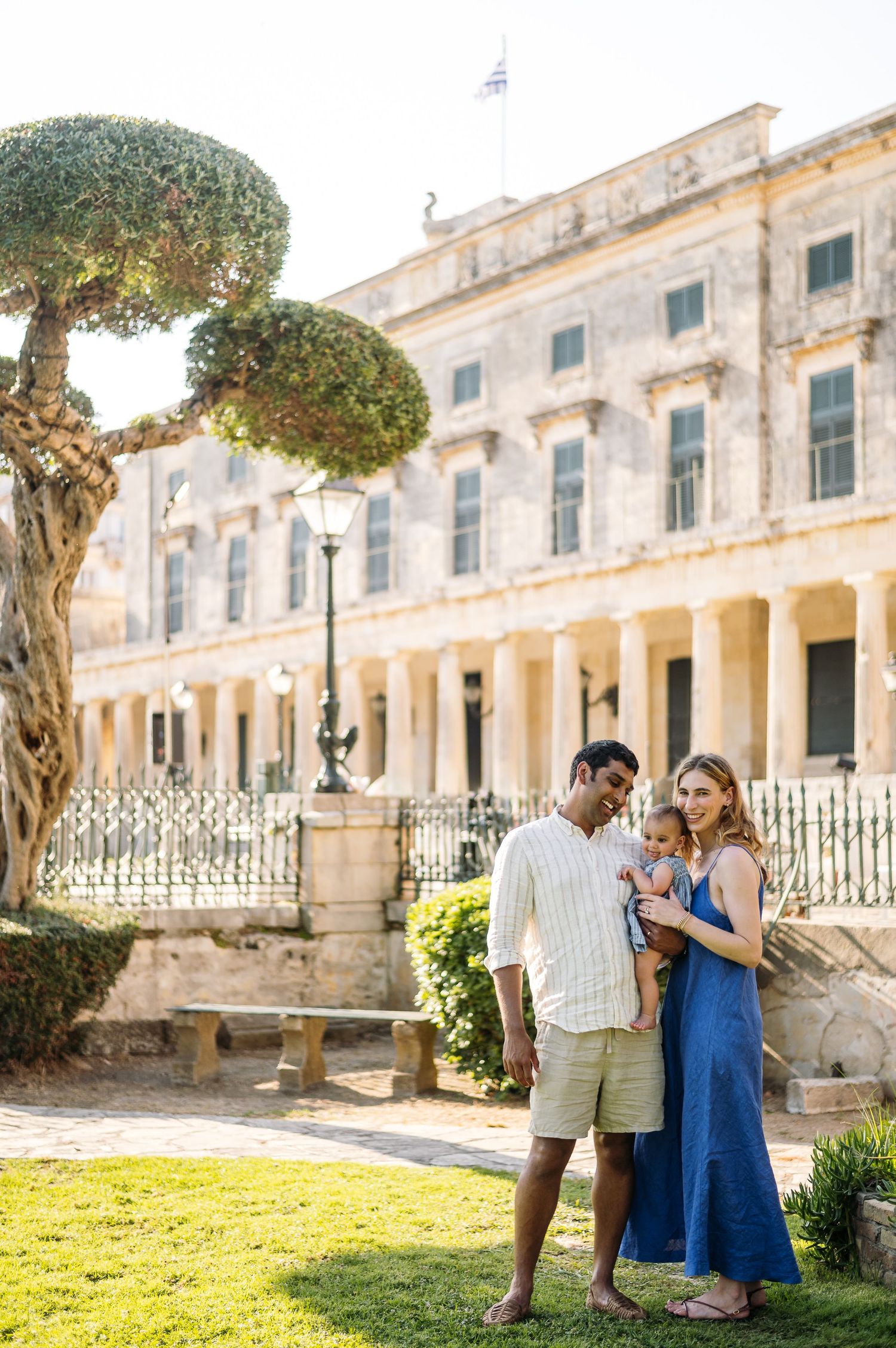 Couple standing in front of historic building with manicured trees and classical architecture.