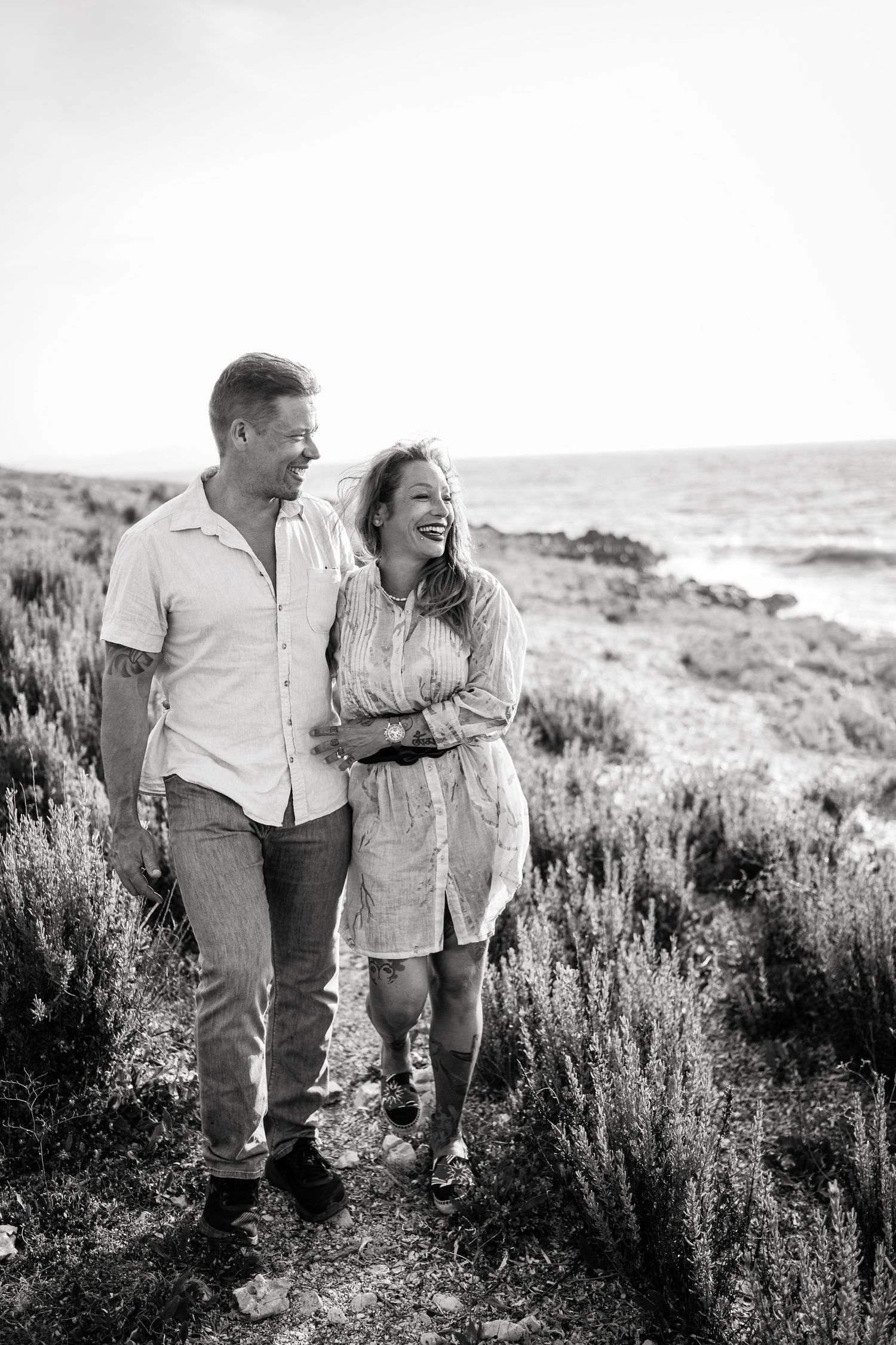 Black and white photo of a couple walking and laughing together through coastal vegetation.