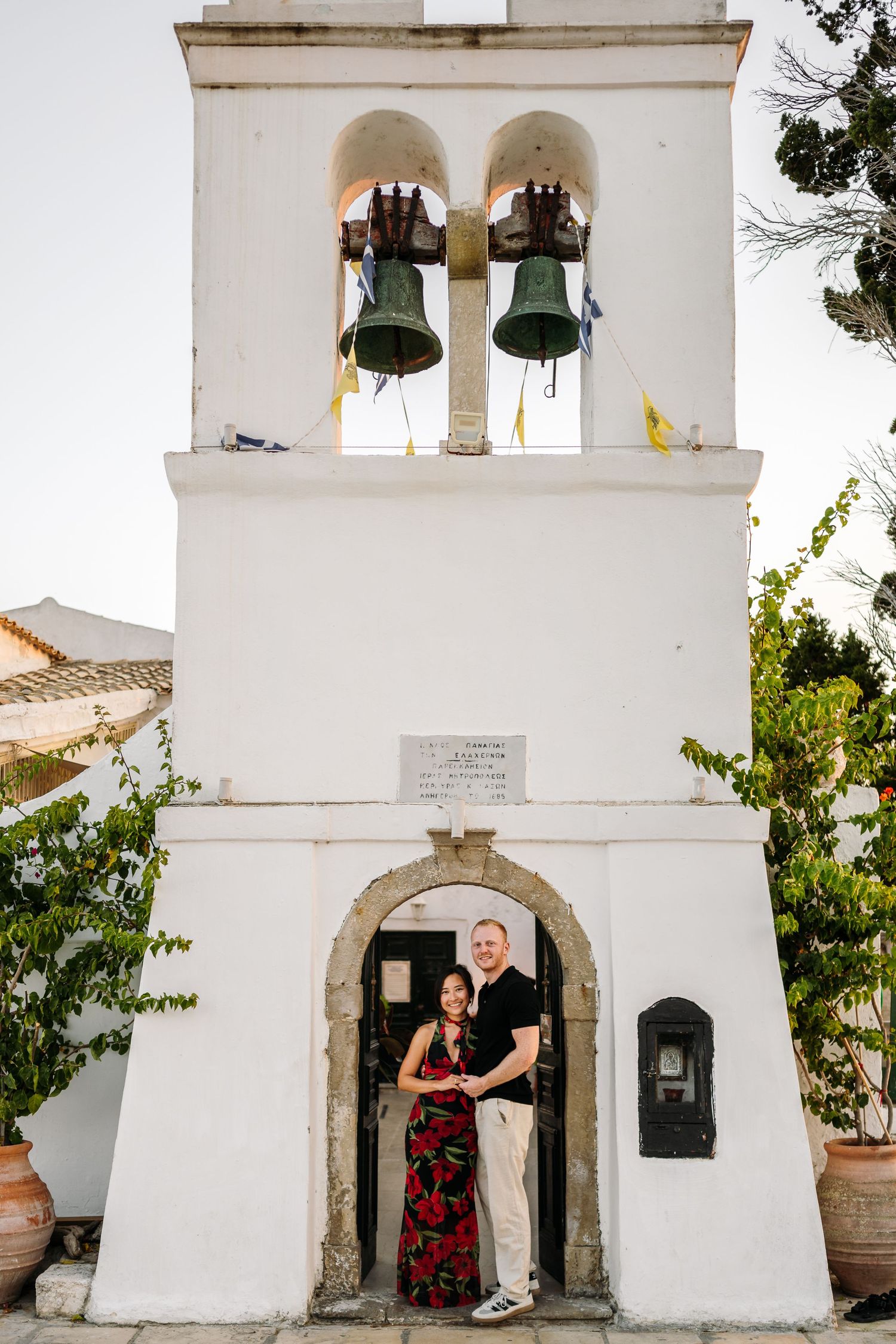 A couple standing in the archway of a white Mediterranean bell tower.