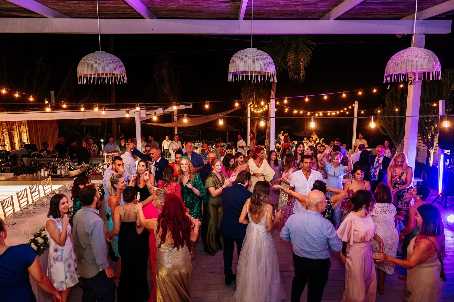 Wedding reception dance floor illuminated with purple lighting and string lights.