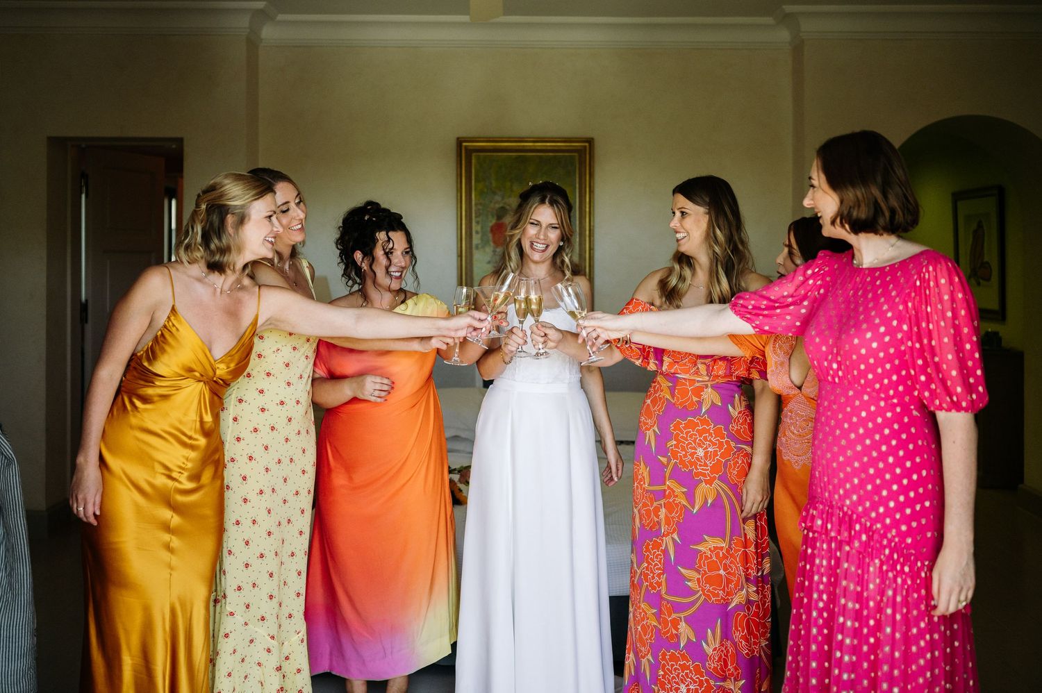 Wedding party in vibrant yellow, orange, and pink dresses celebrating together.