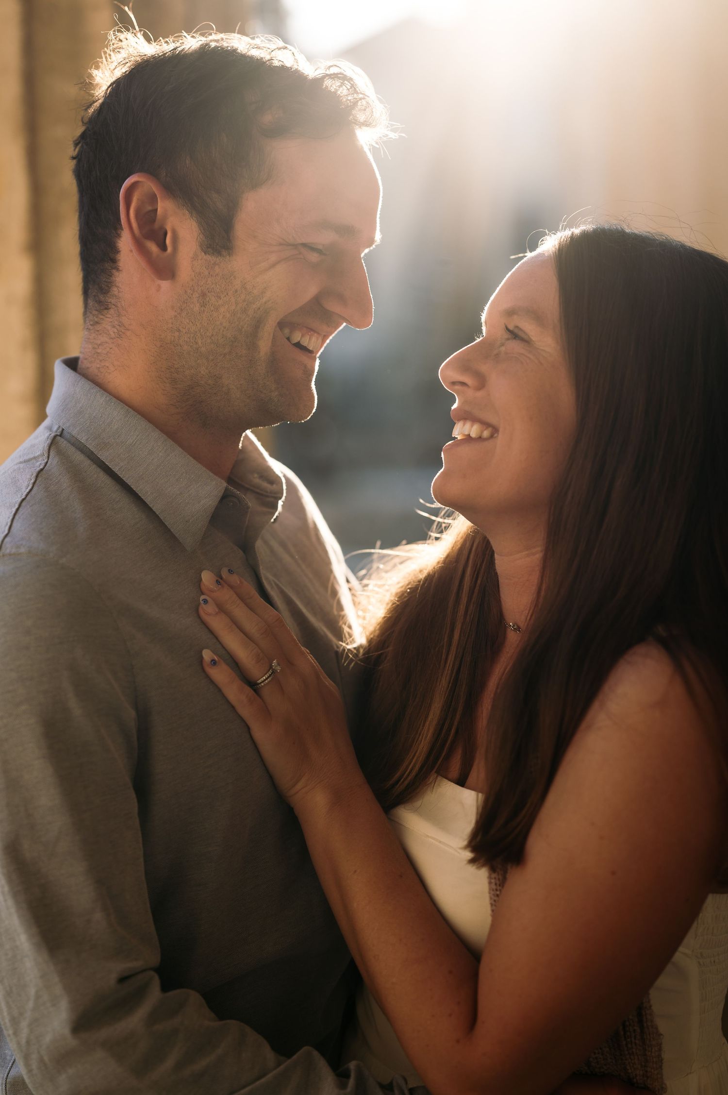 An intimate close-up portrait of a couple laughing together in warm sunlight.