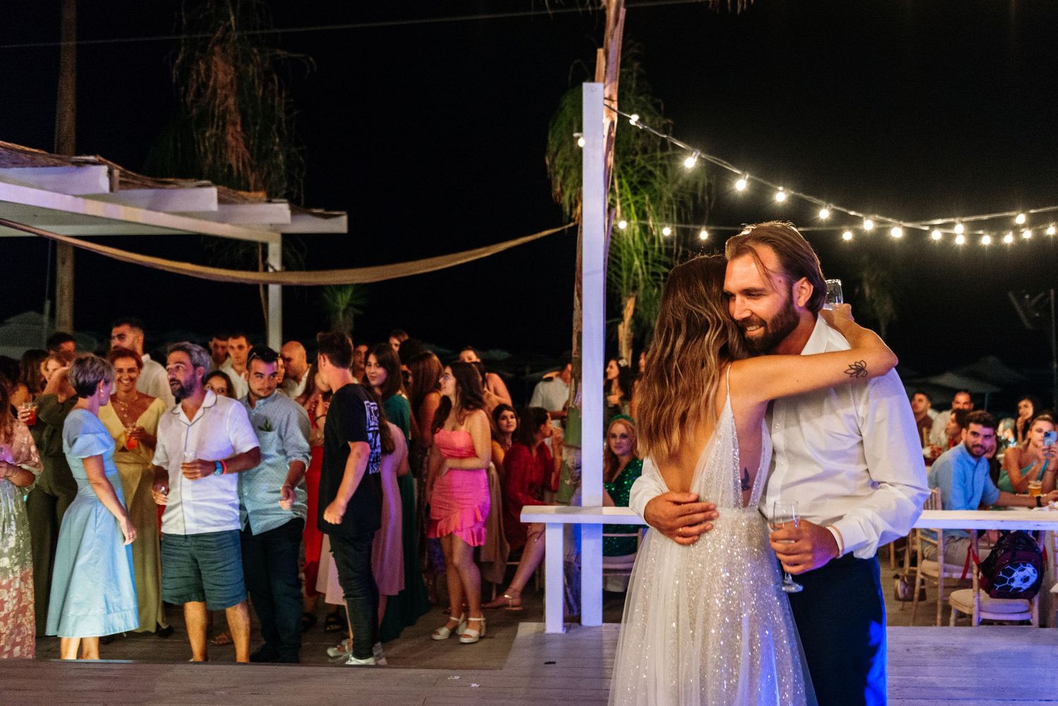 Wedding guests dance and celebrate on an outdoor dance floor under string lights at night.