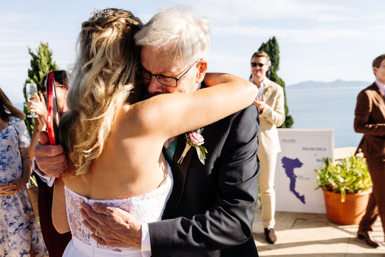 Romantic outdoor celebration with guests dancing and embracing under blue skies.