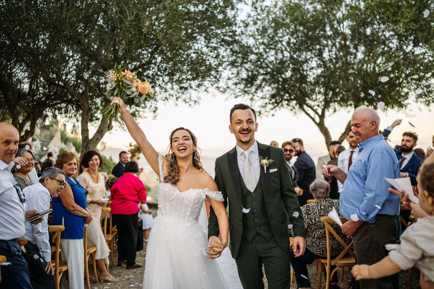 Joyful outdoor wedding celebration with guests under natural tree canopy.