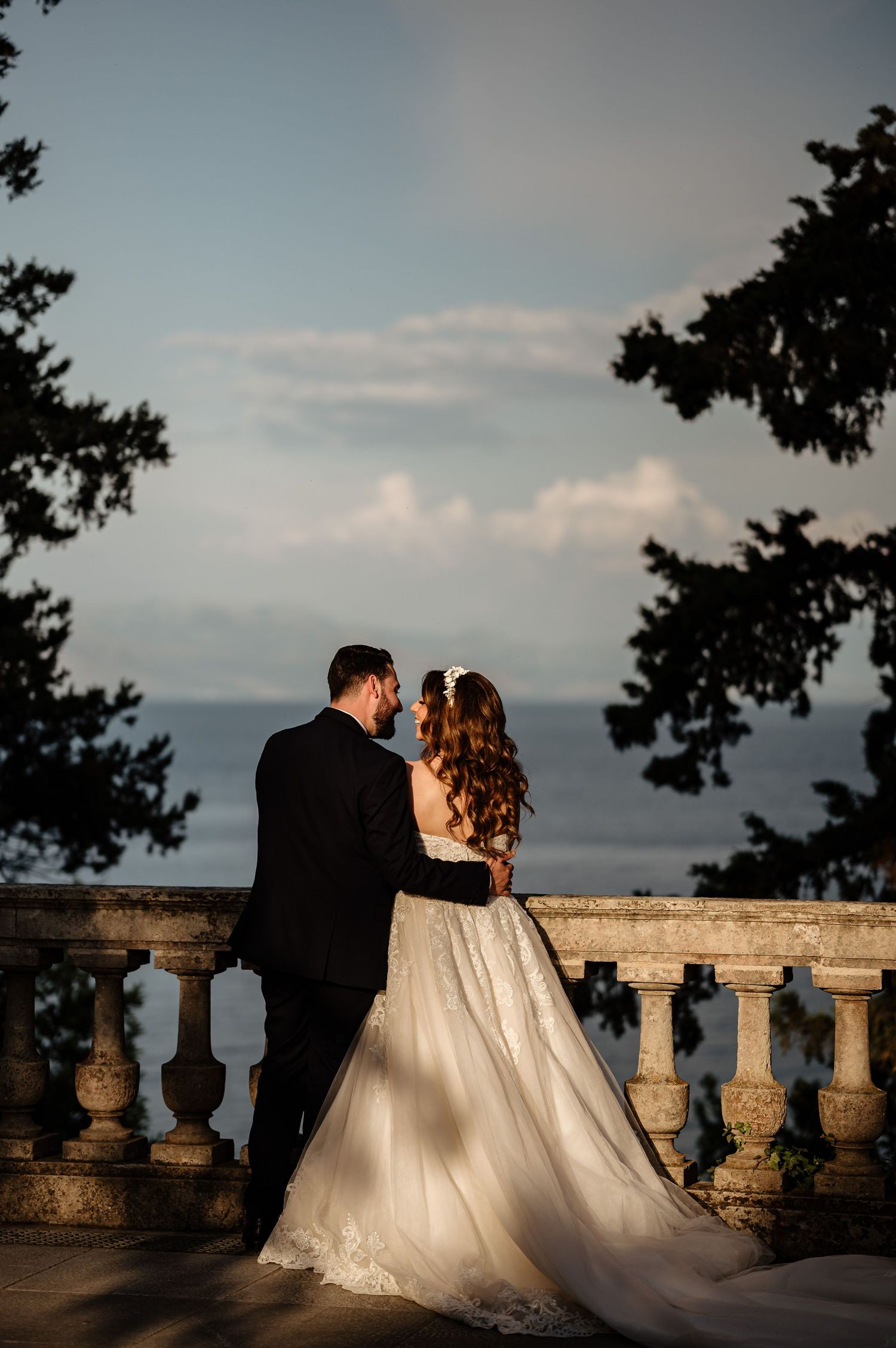 Sunset wedding portraits on a stone balcony with dramatic lighting and ocean views.