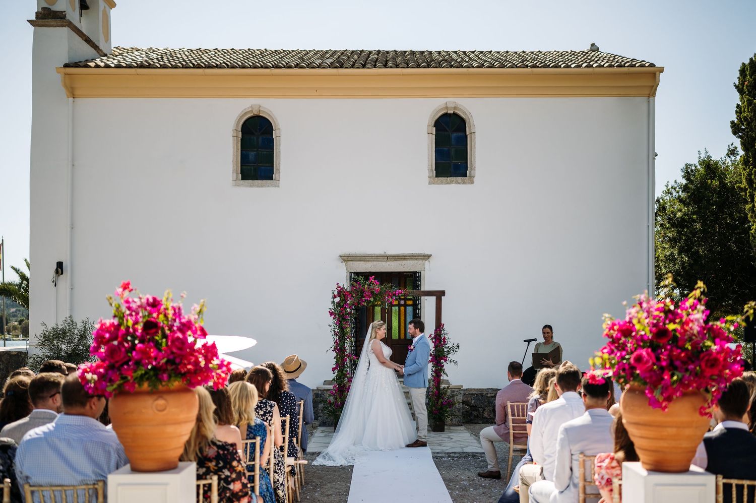 White church facade adorned with bright pink bougainvillea flowers in terra cotta pots.