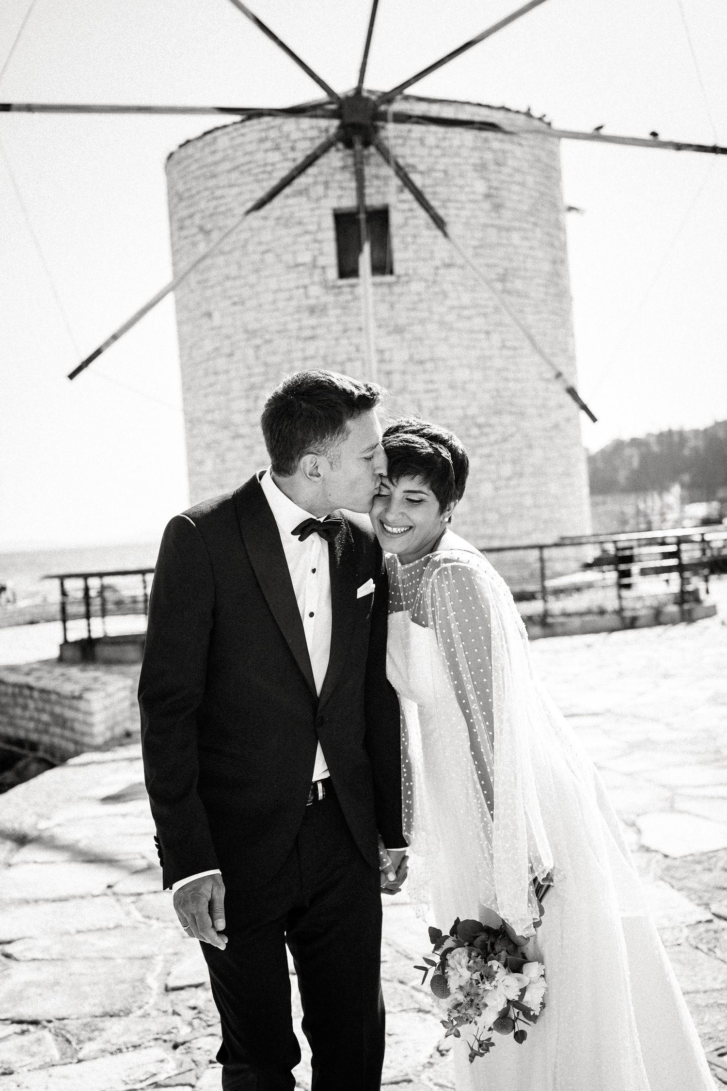 Black and white wedding photos show a couple posing romantically in front of traditional windmills.