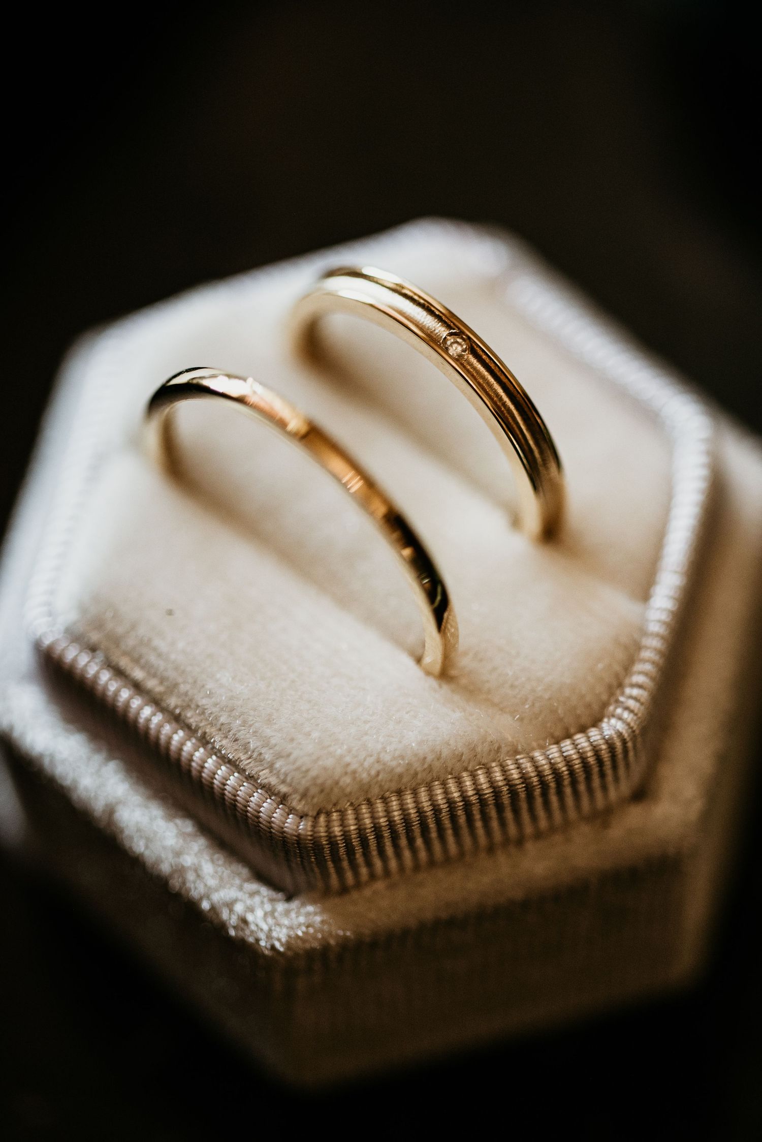 Two gold wedding bands rest on a textured hexagonal ring box.