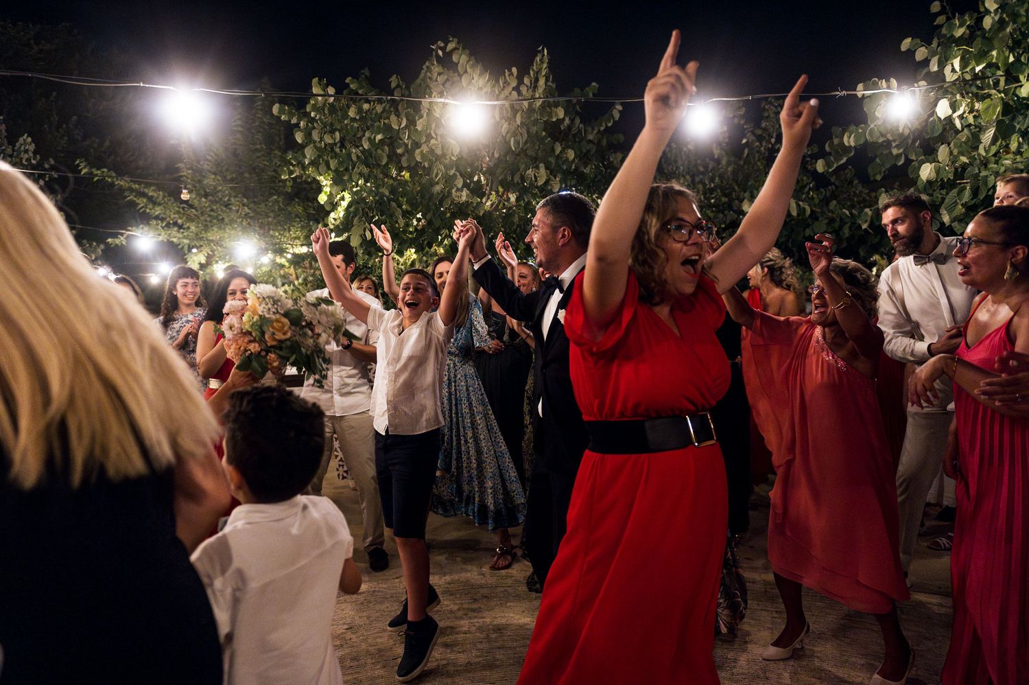Wedding guests dancing and celebrating on an outdoor dance floor under string lights at night.