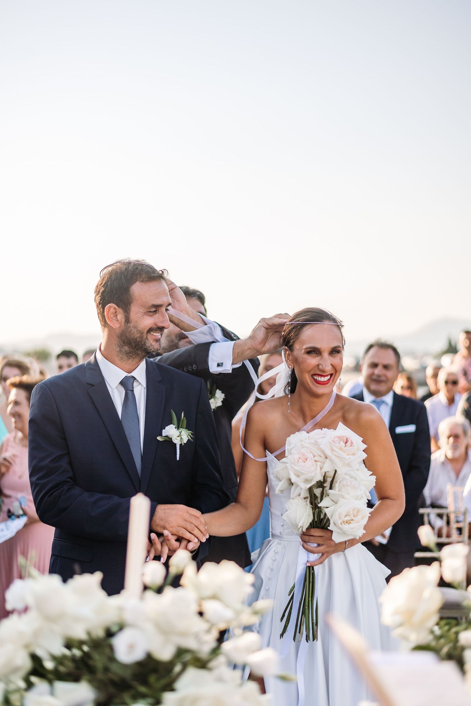 Joyful wedding celebration with guests laughing outdoors surrounded by white flowers.
