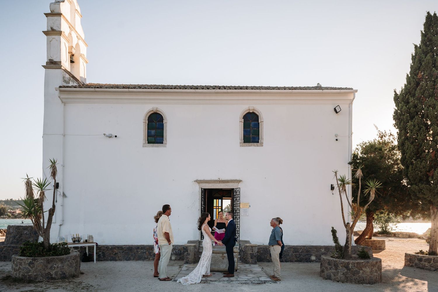 A traditional white Mediterranean church with wedding guests gathering outside.
