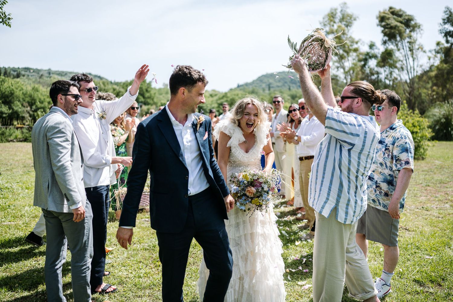 Wedding party celebrates with champagne on a grassy hillside.