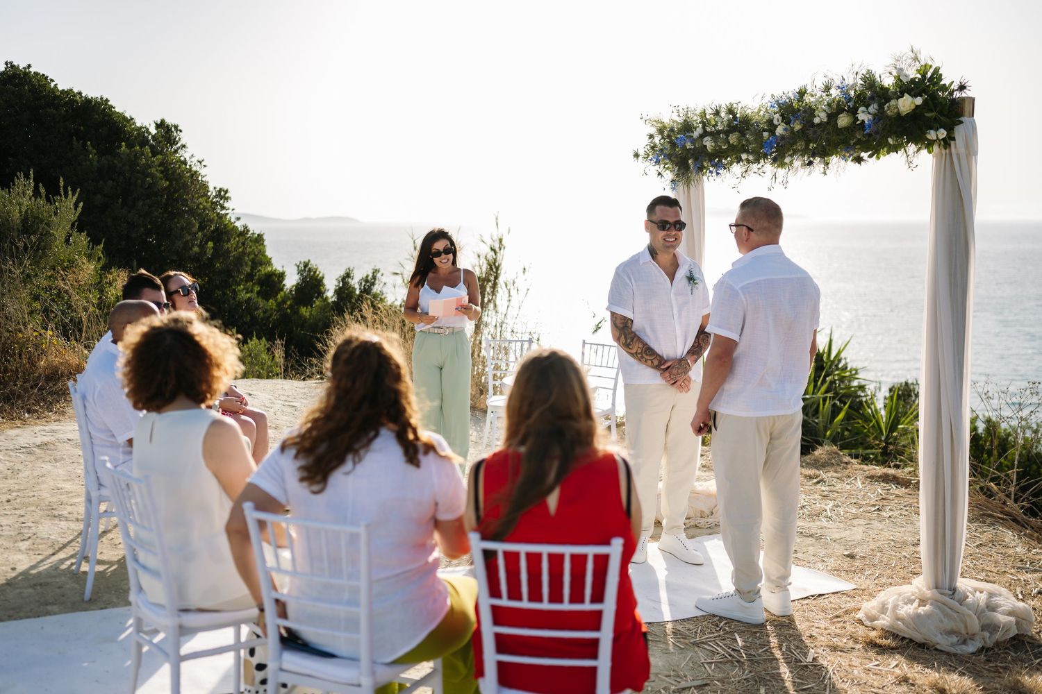 Outdoor beach wedding ceremony setup with white chairs and floral arch overlooking the ocean.