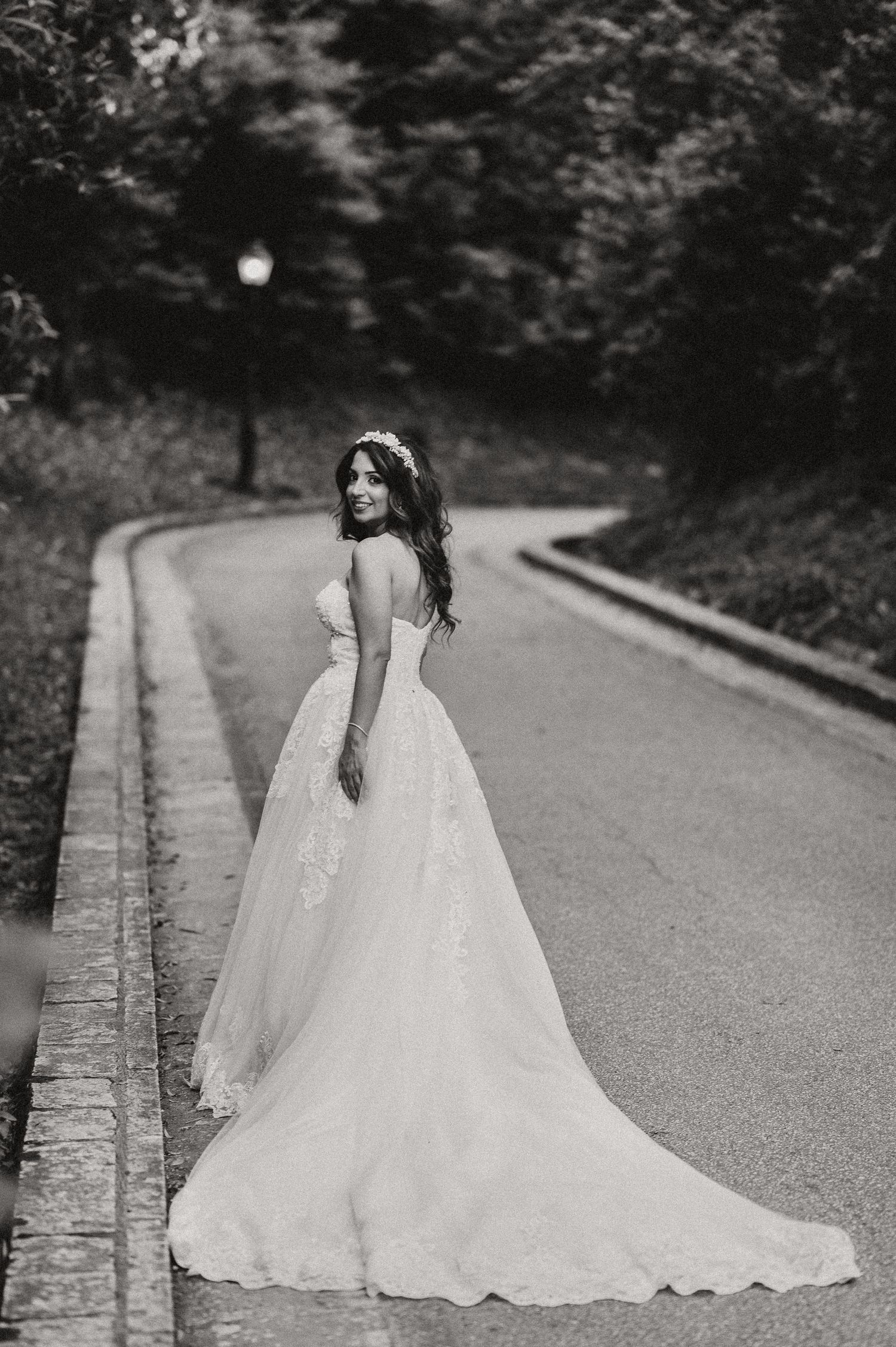 Bride in flowing white gown walks along a curved garden path.