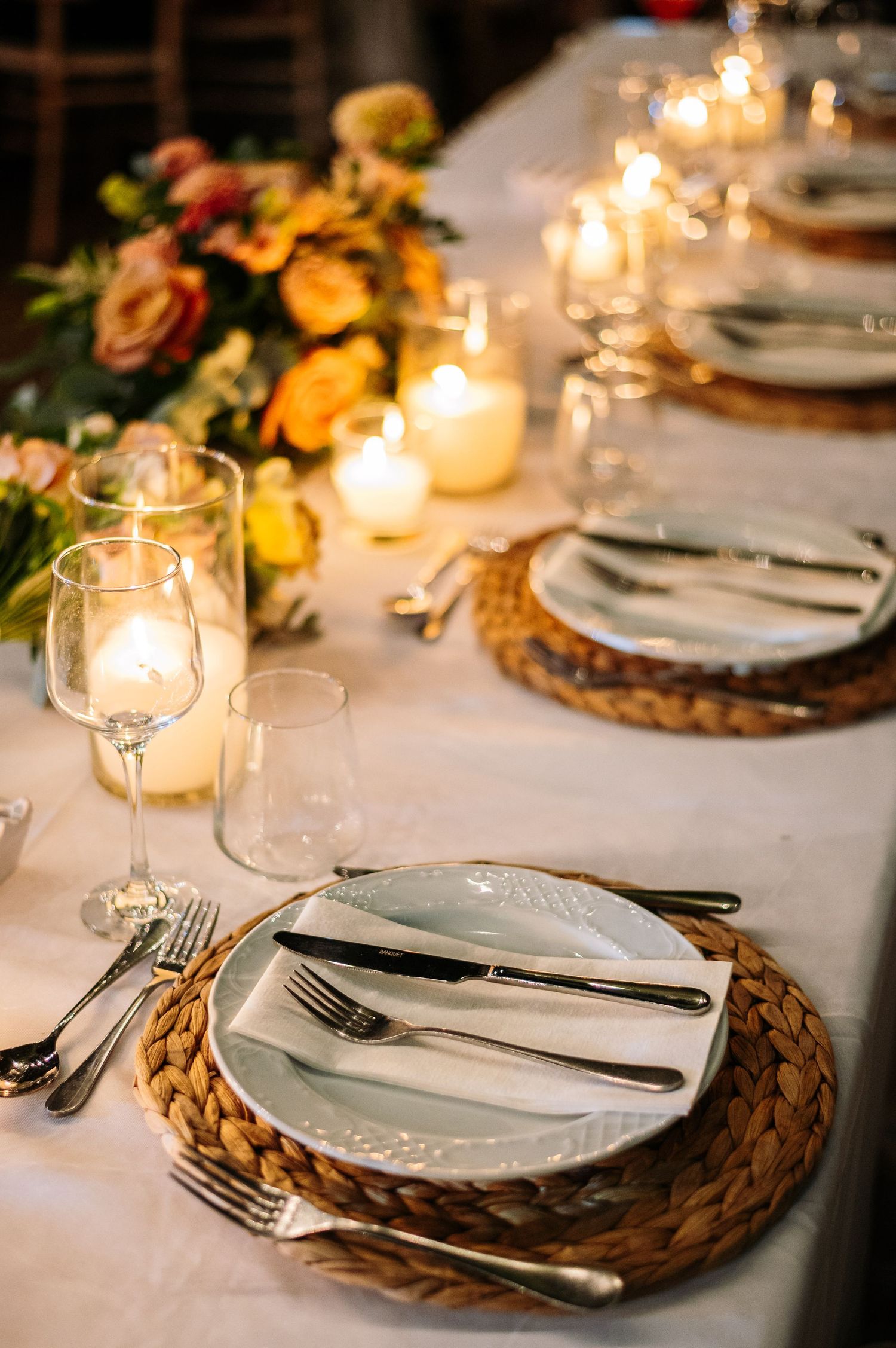 Intimate wedding table settings with woven chargers, white plates and candlelight.