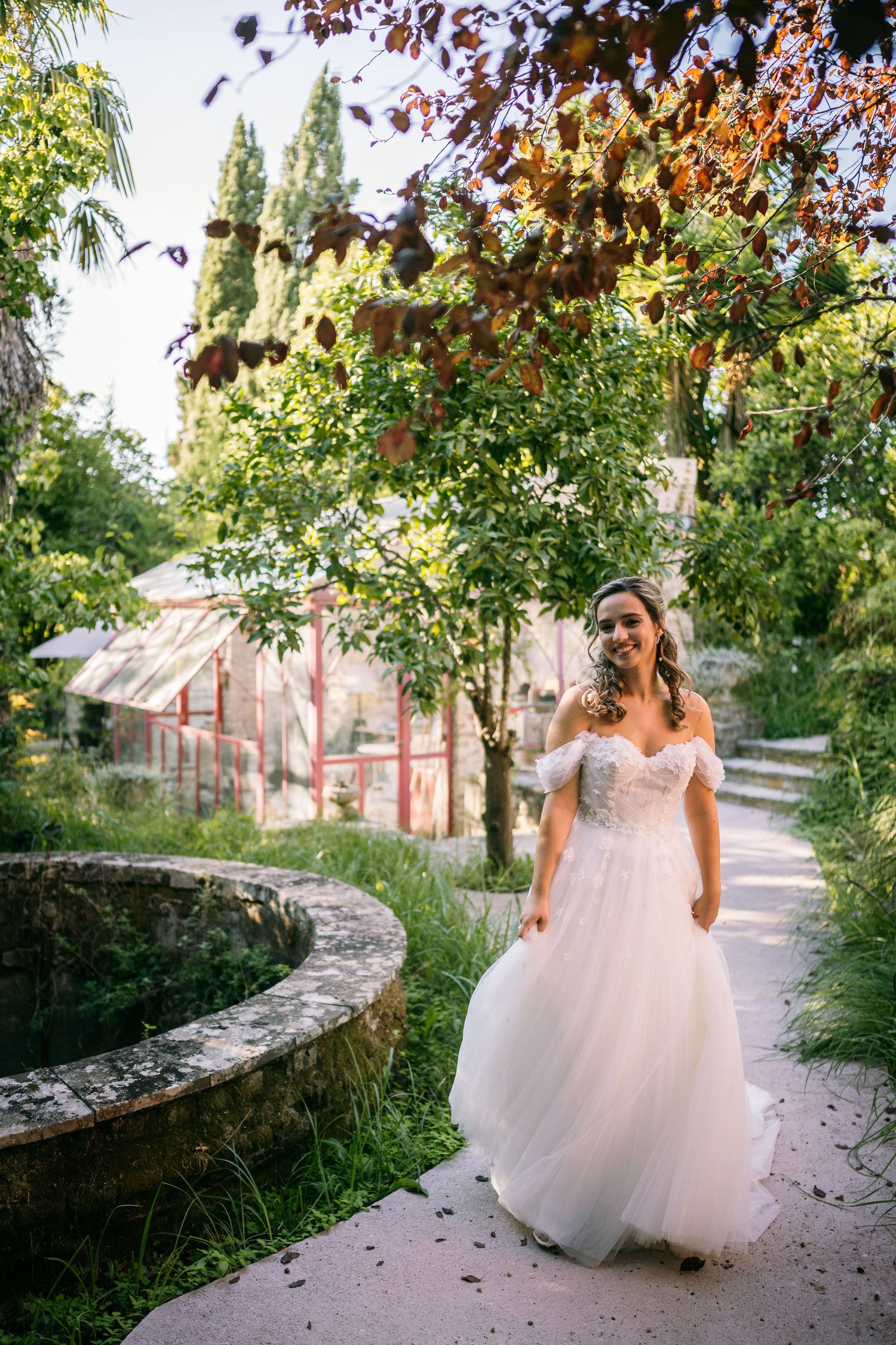 A flowing white wedding dress moves through an autumn garden path with stone walls.