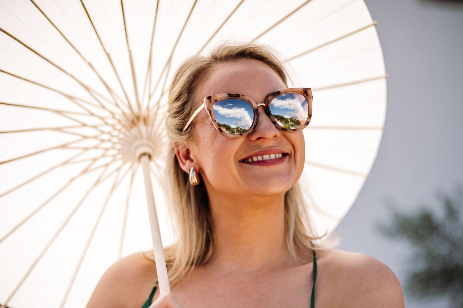 Woman with reflective sunglasses and white parasol smiling in bright sunlight.