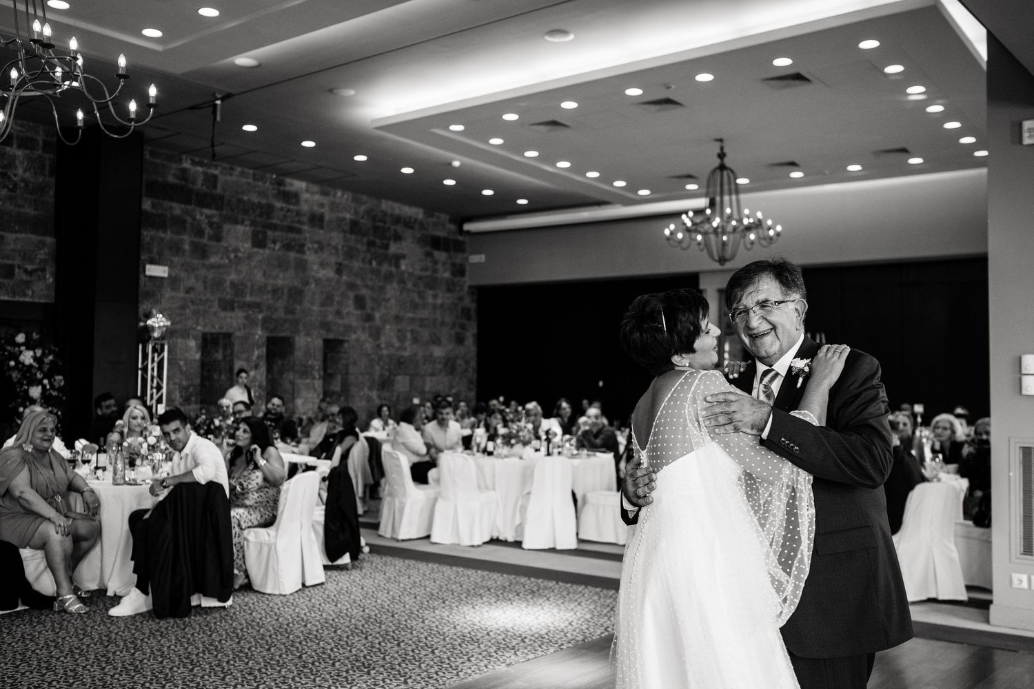 Black and white panoramic shot of a wedding reception venue with elegant chandeliers and table settings.