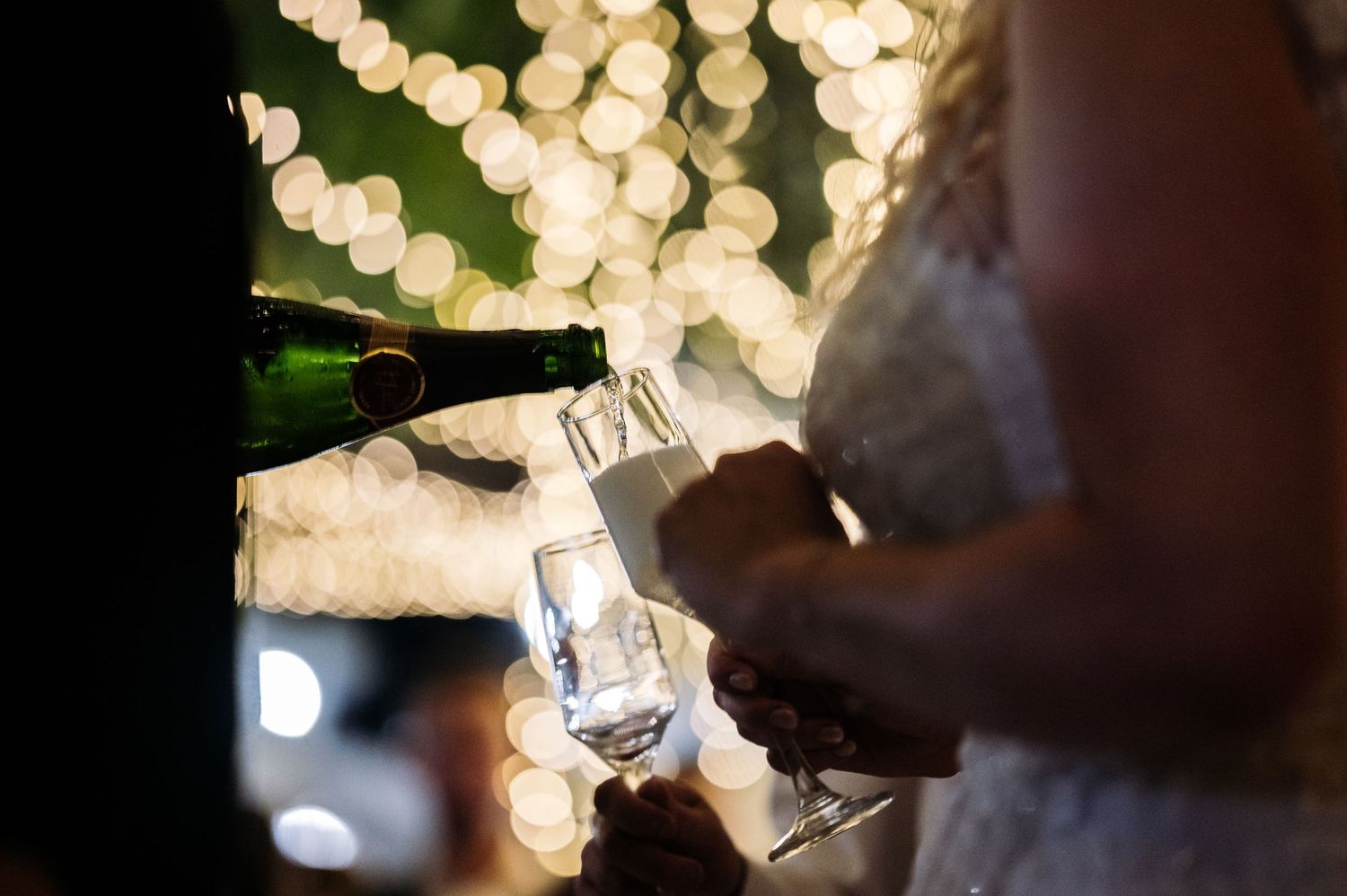 Champagne being poured into glasses with sparkling lights in the background.