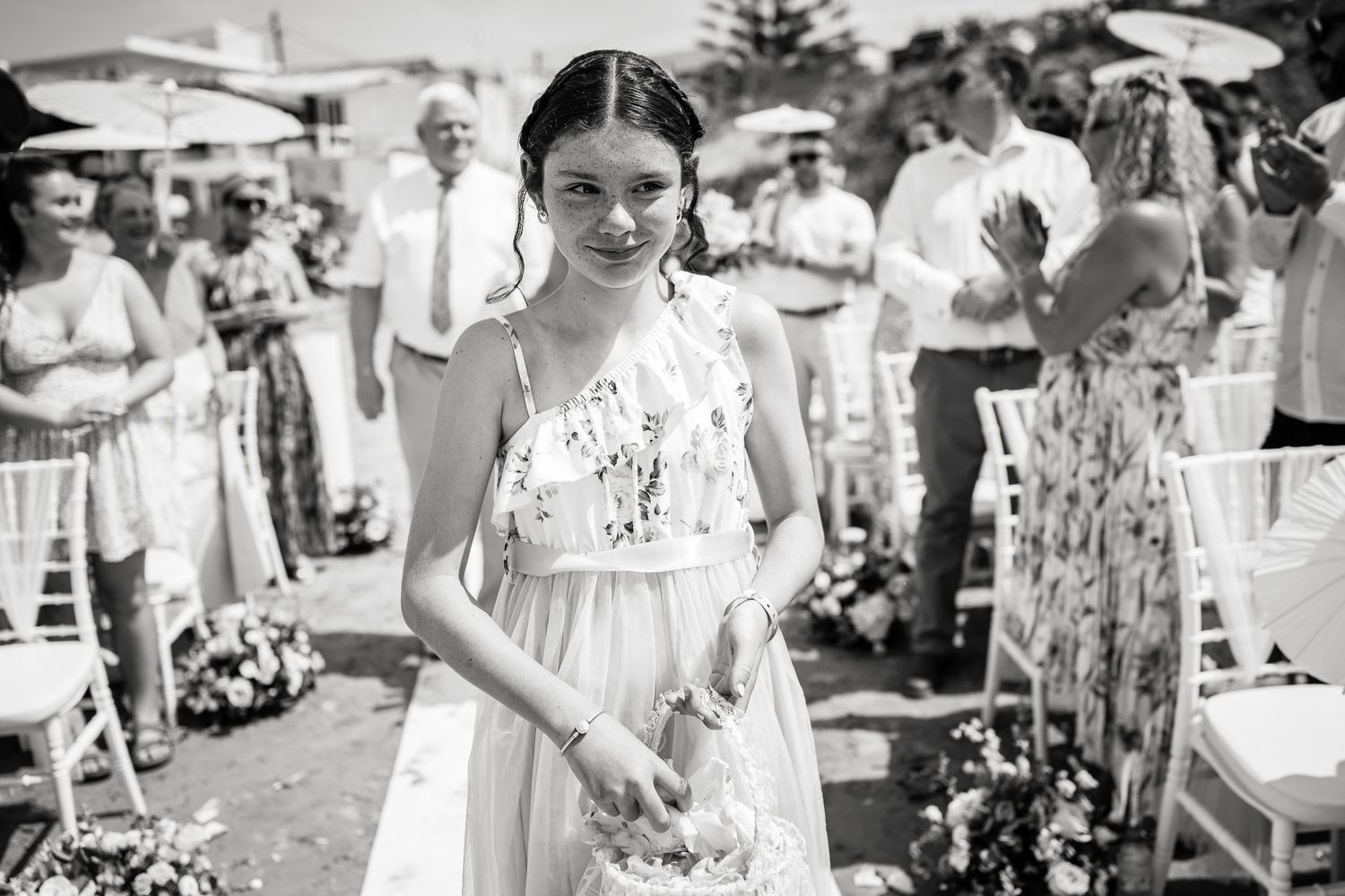 Wedding guests gather at an outdoor beach ceremony under bright skies.