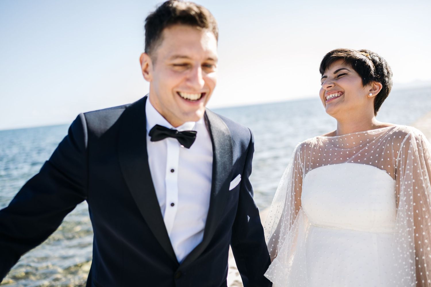 A cheerful wedding couple shares laughter during their seaside photoshoot.