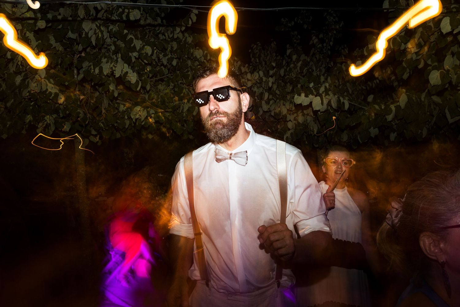 Golden light trails create patterns above dancing wedding guests at night.