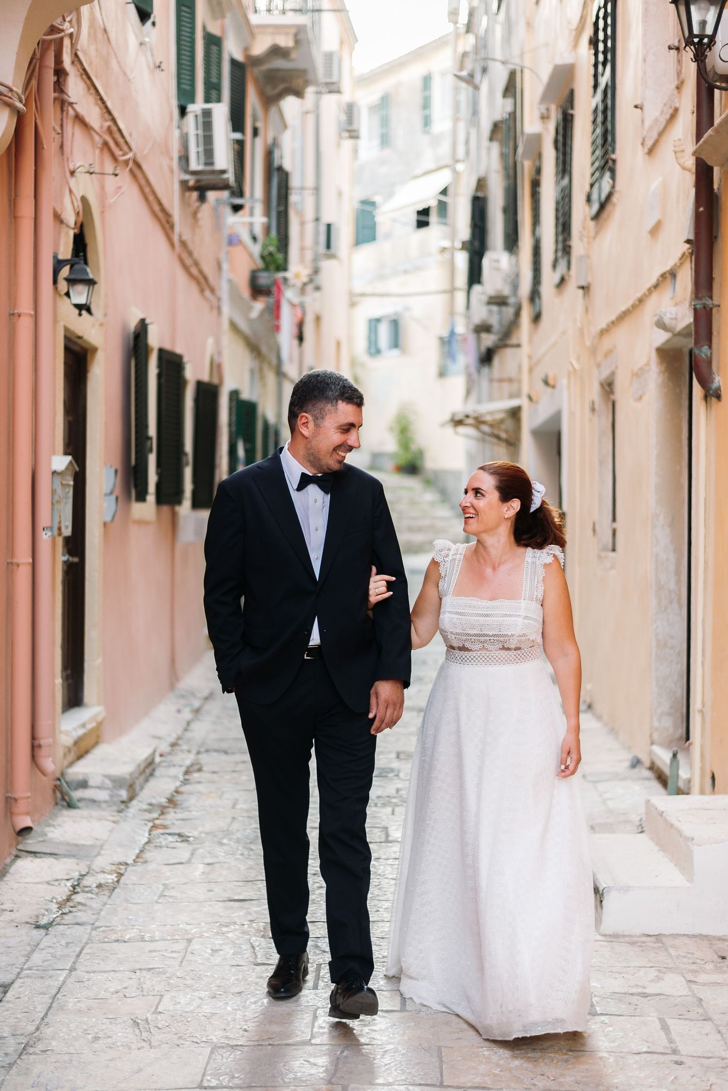 Wedding couple walking through charming European streets with pink buildings.
