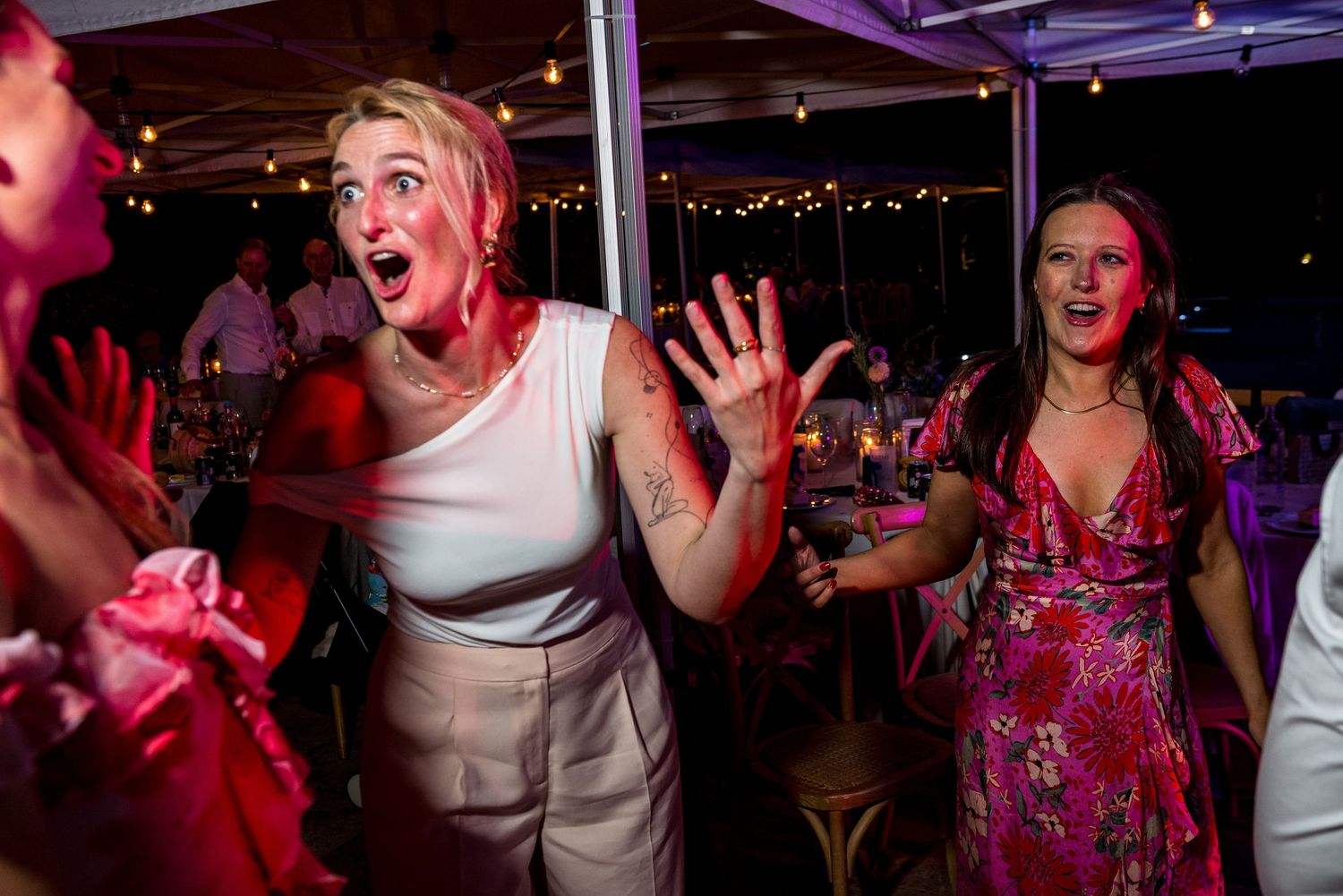 Party guests dancing and celebrating under dramatic pink and purple lighting.