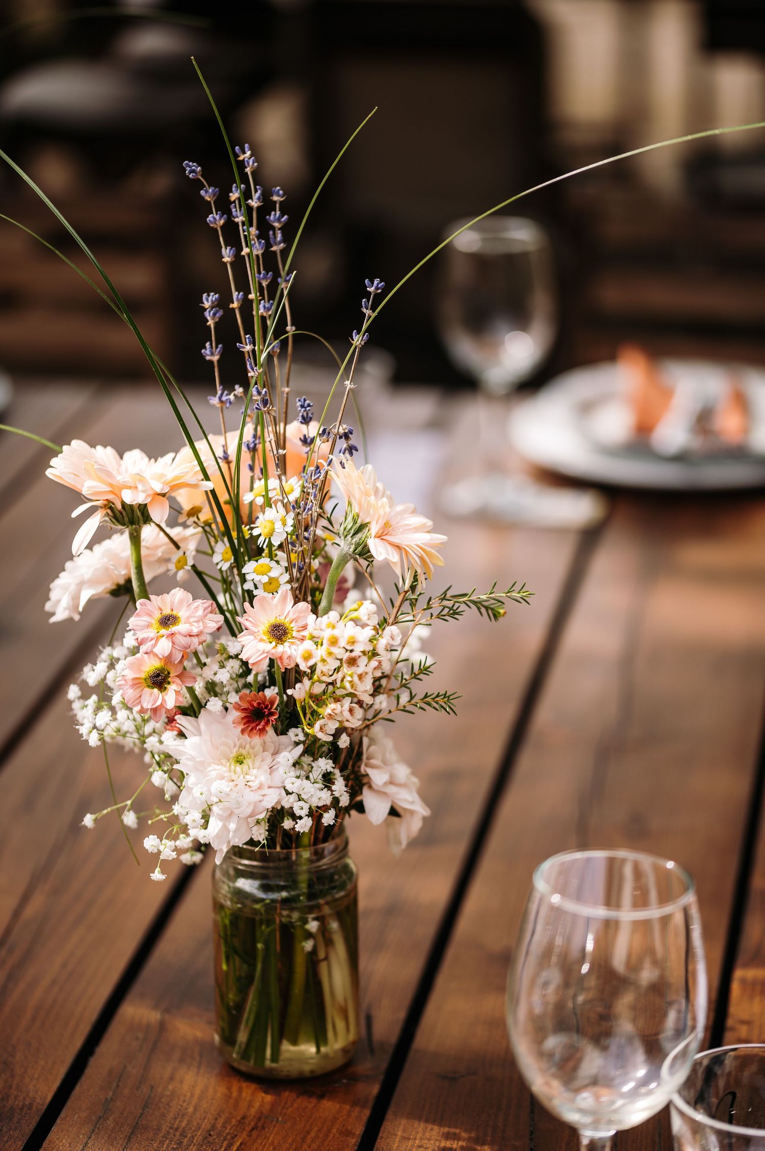 Delicate wildflower centerpieces in mason jars on wooden tables.