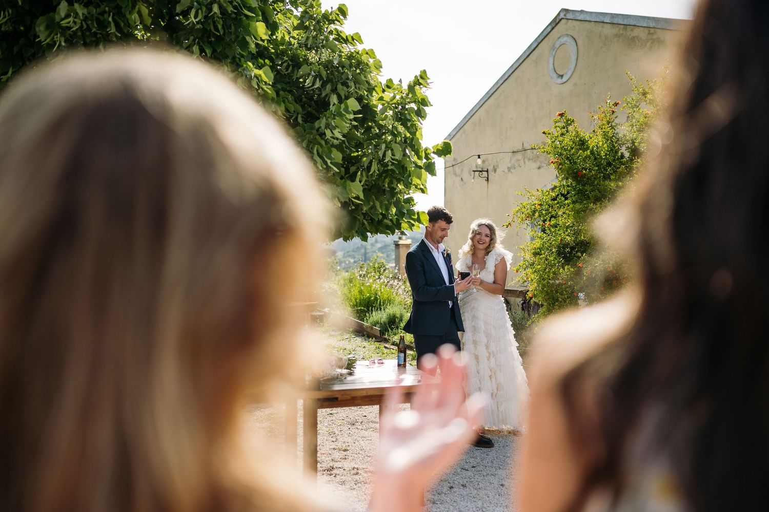 Wedding ceremony guests watch couple in outdoor garden setting.