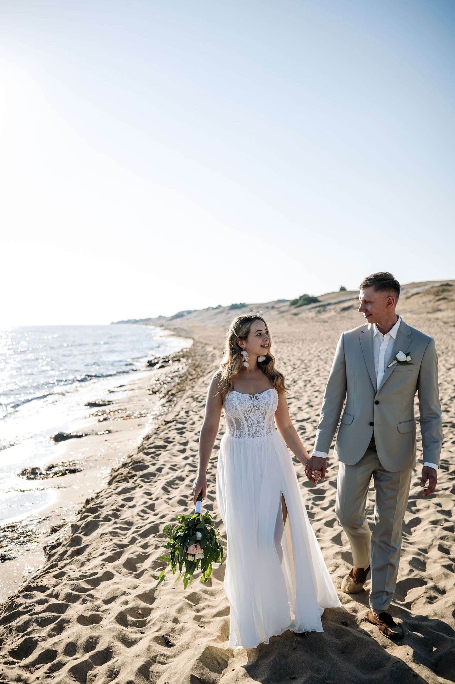 Newlyweds walking along scenic beach shoreline after ceremony.