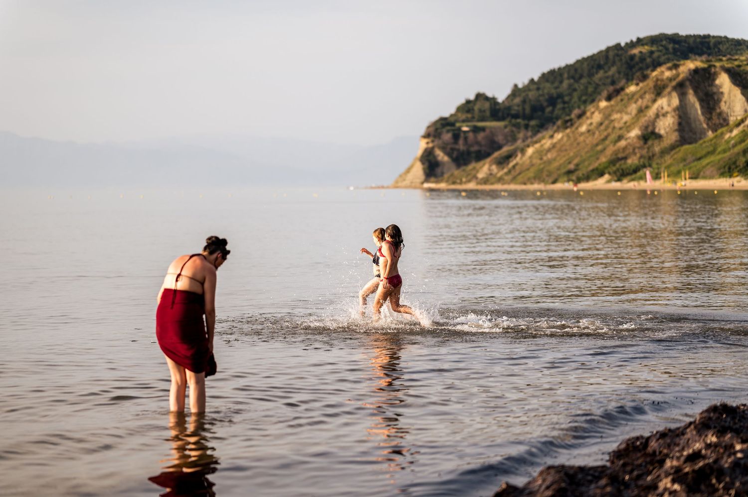 Scenic coastal cliffs and beach landscape with people wading in calm ocean waters.