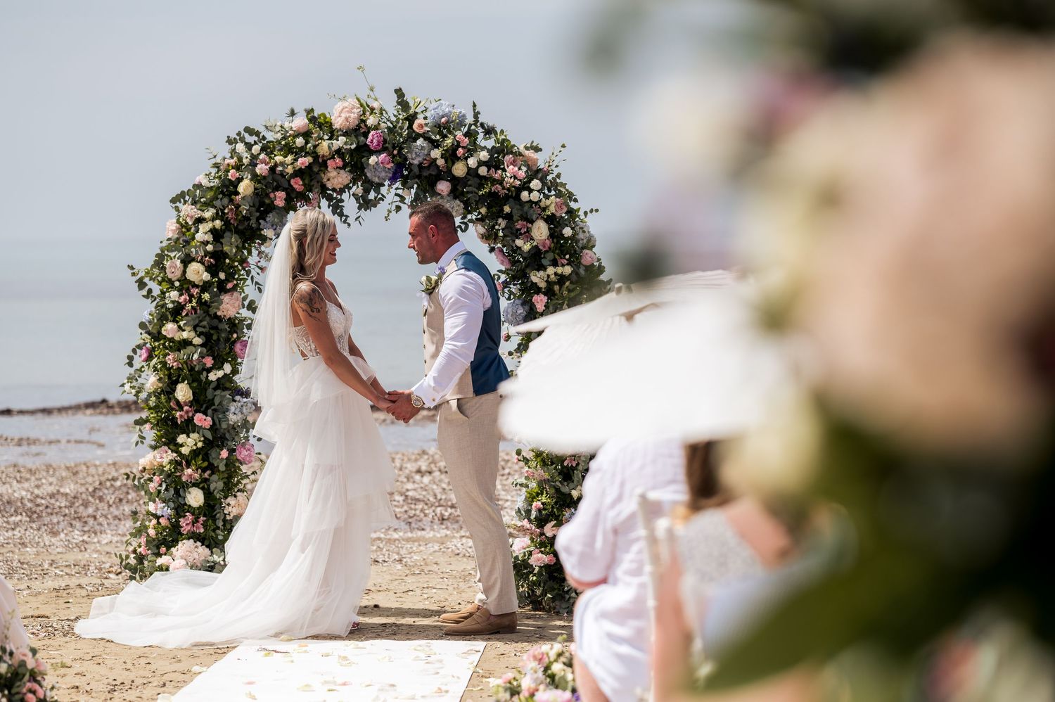 Wedding ceremony setup with floral arch and white chairs on beach.