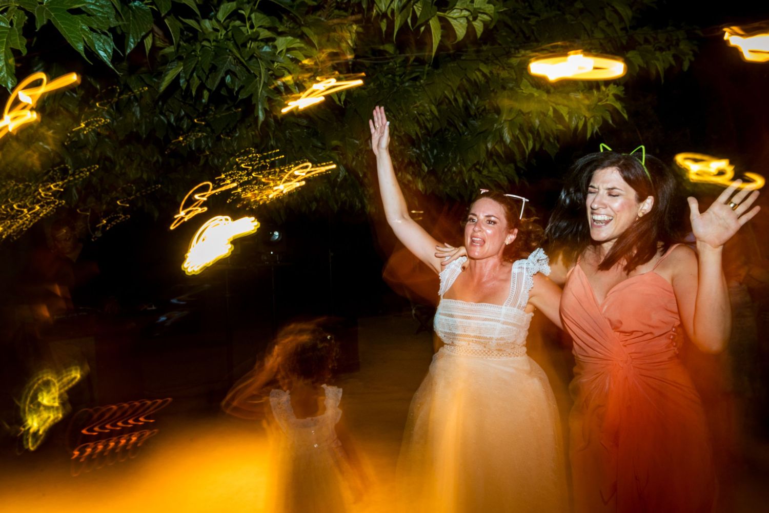Wedding guests dance beneath warm string lights at an outdoor evening celebration.