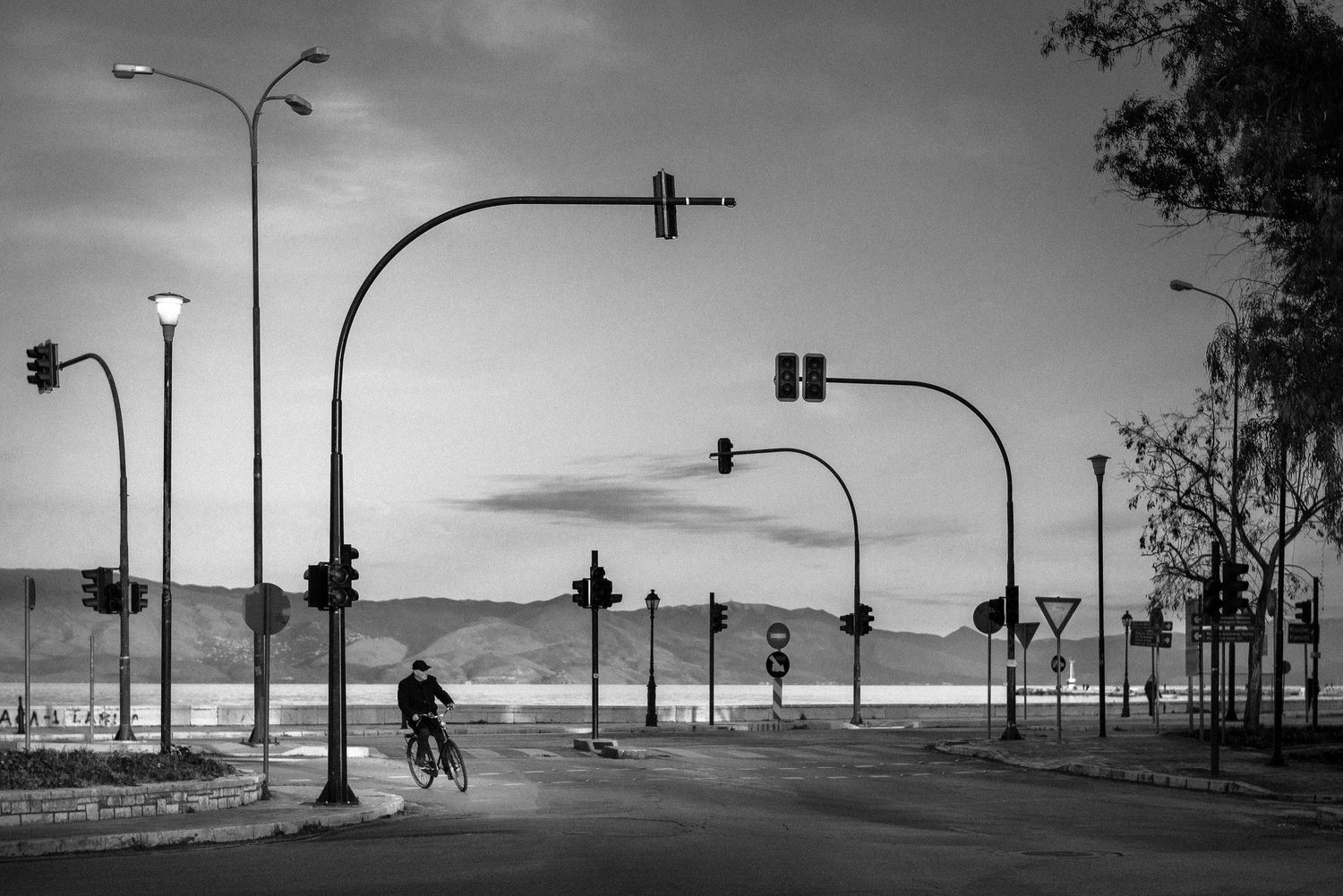 Silhouettes of cyclists against a dramatic sky with street lamps and traffic signals.