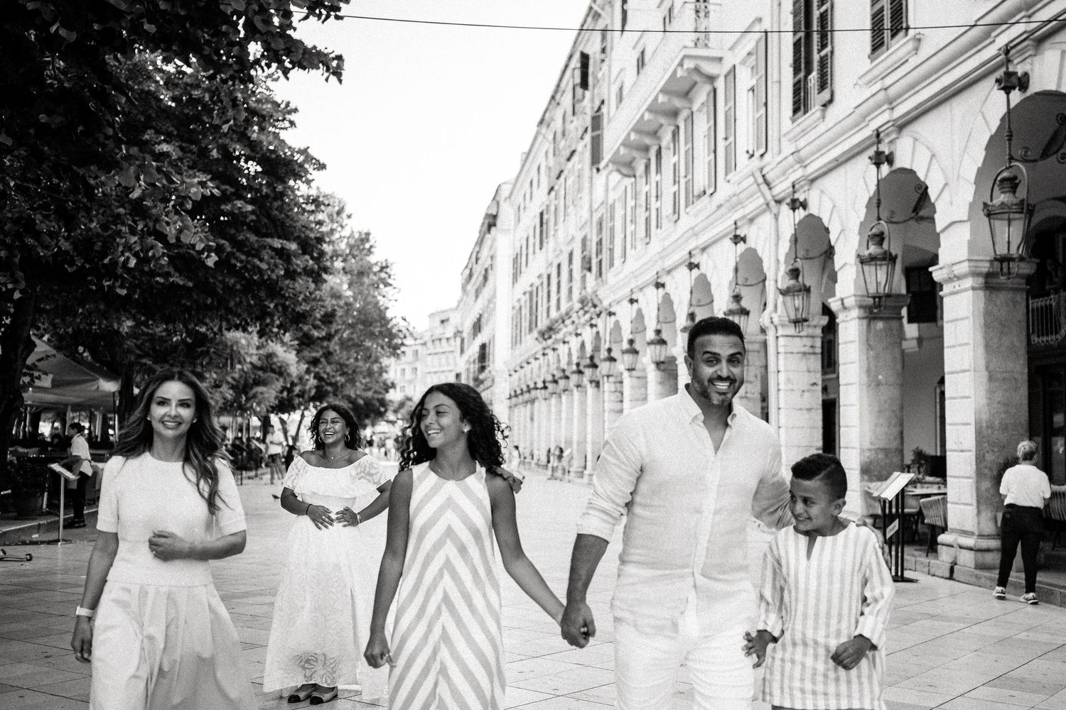 Black and white photo of a family walking and playing along an elegant covered walkway.