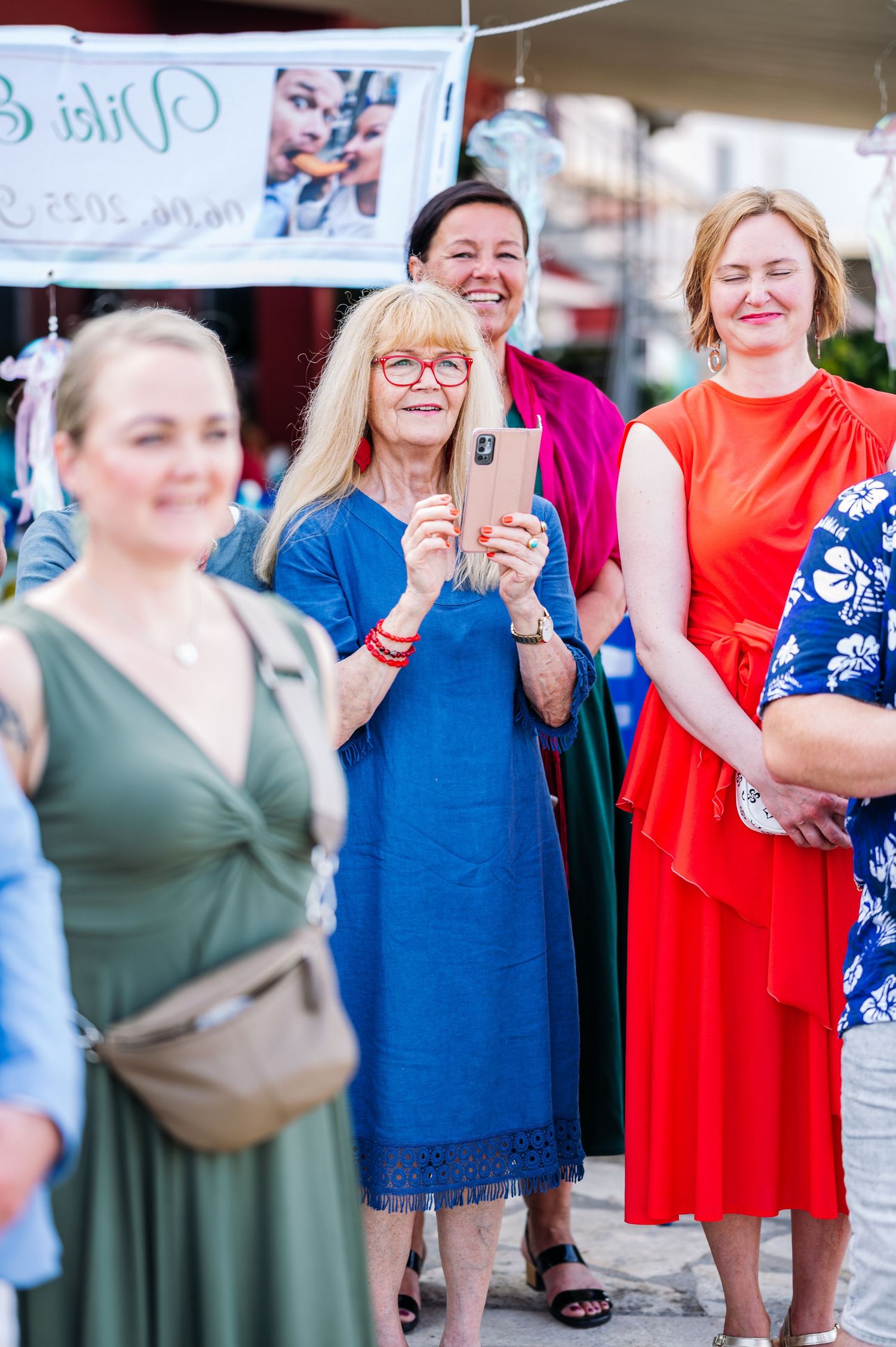 Wedding guests in colorful dresses share joyful reactions during an outdoor celebration.