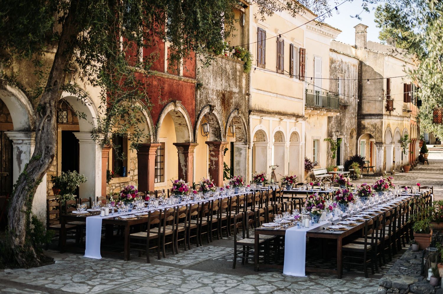 Long outdoor wedding reception tables set up in rustic Mediterranean courtyard.