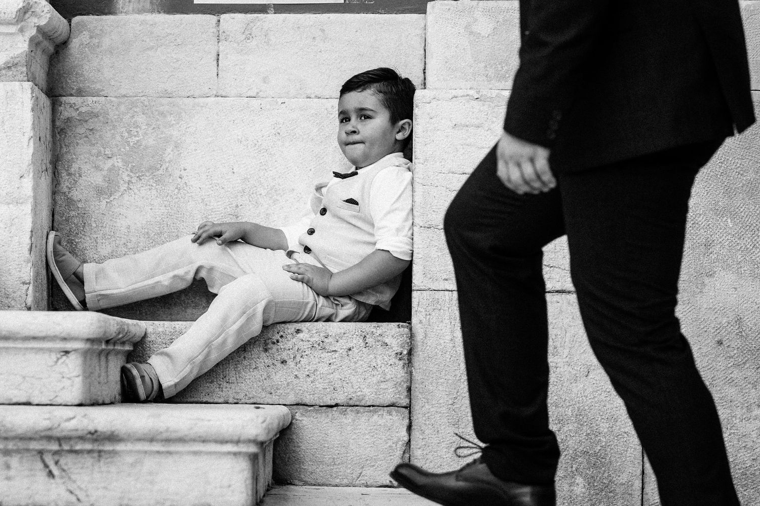 Wedding party members sitting casually on stone steps in formal attire.