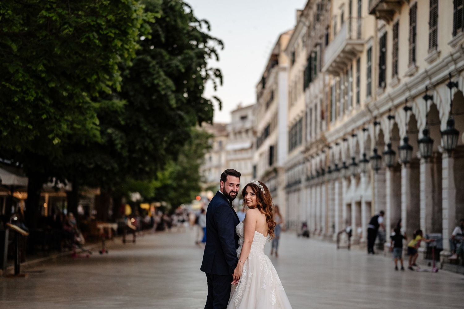 A couple stands on a historic European street lined with classical architecture and columns.