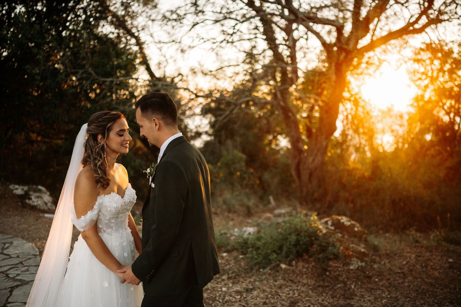 Wedding couple posing against dramatic sunset backdrop in natural outdoor setting.