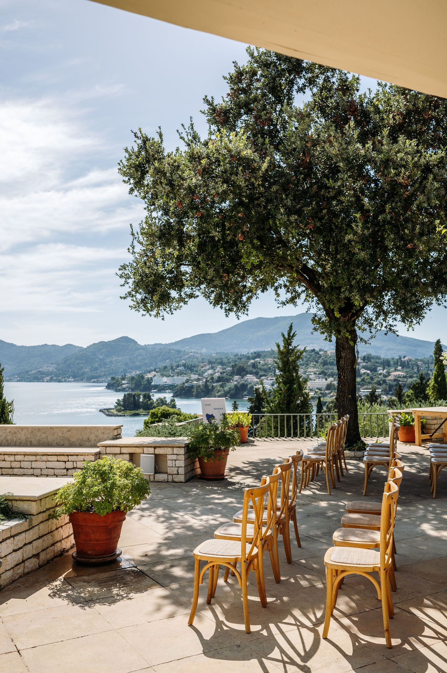 Mediterranean terrace with wooden chairs and tables offering panoramic views of a coastal bay.