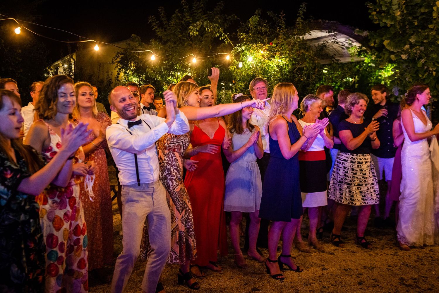 Wedding guests dancing under string lights at an outdoor evening celebration.
